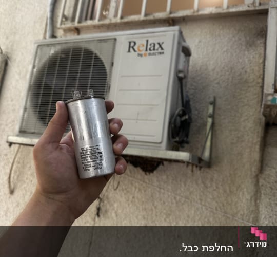 יד מחזיקה רכיב מול מזגן על קיר חיצוני